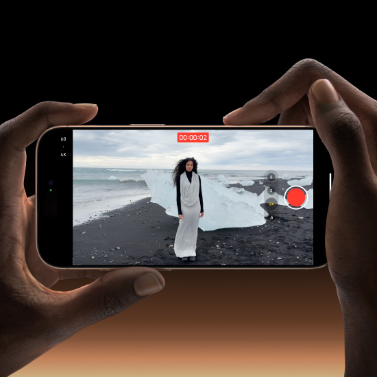 A person holding the iPhone 16 Pro Max while recording a high-resolution video of a model on a black sand beach, showcasing its advanced cinematic video capabilities.
